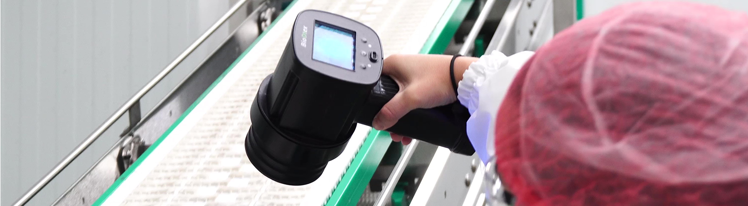 Worker using a BioDtex UV detection device to inspect a conveyor belt for hidden biofilm contamination
